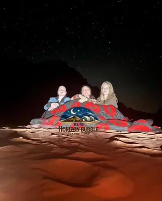 a group of three people sitting on a bed in the desert at RUM HORIZON BUBBlE LUXURY CAMP in Wadi Rum