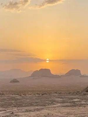 a sunset in the desert with mountains in the background at سفينة الصحراء وادي رم in Disah