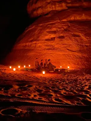 a group of three people sitting on a beach with candles at سفينة الصحراء وادي رم in Disah