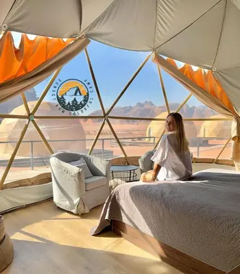 a woman sitting on a bed in a tent at WADI RUM BUBBlE AOSE CAMP in Wadi Rum