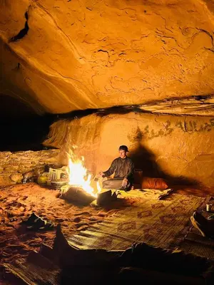 a man sitting next to a fire in a cave at Wadi Rum Wanderer cmap in Wadi Rum