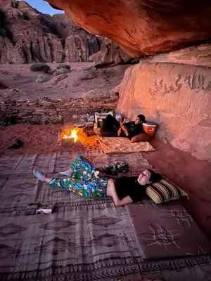 a group of people laying around a fire in a cave at Wadi Rum Wanderer cmap in Wadi Rum