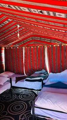 a room with three beds and a red wall at Desert Nights camp in Wadi Rum