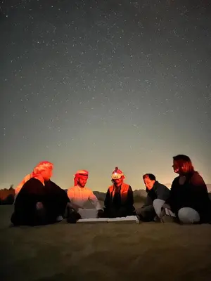 a group of people sitting in the desert at night at عماد رم in Wadi Rum