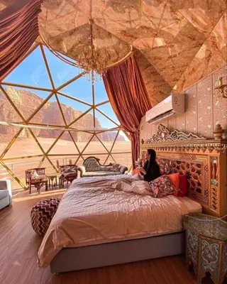 a woman sitting on a bed in a room with a large window at عماد رم in Wadi Rum