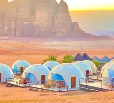 a group of tents in the desert with a mountain in the background at Wadi Rum, the best stars in Wadi Rum
