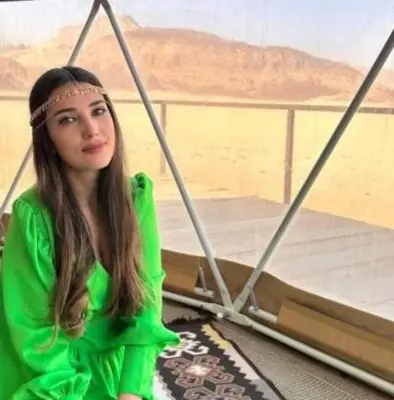 a girl in a green dress sitting next to a bed at Wadi Rum Salem in Wadi Rum
