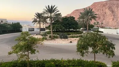 an empty parking lot with palm trees and a mountain at Luxury Suite in Aqaba AlRaha Village Marsa Zayed in Aqaba
