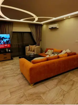 an orange couch in a living room with a tv at روف طابق ثاني تشطيب فندقي باطلاله ساحرة بعمارة عائلات بعبدون الشمالي in Amman