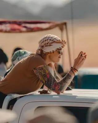 a woman with tattoos on her arm sitting on a table at Wadi Rum Karolina Bubbles camp in Wadi Rum