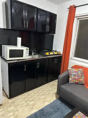 a kitchen with black cabinets and a microwave and a couch at Al Jubaiha cozy studio 2 in Amman