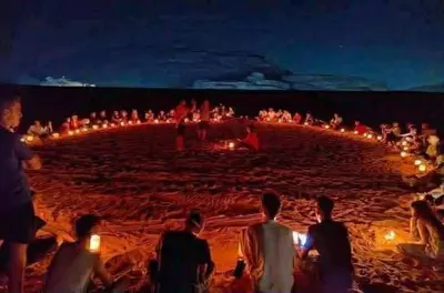 a group of people sitting around a beach at night at Wadi Rum cloud in Ma‘ān