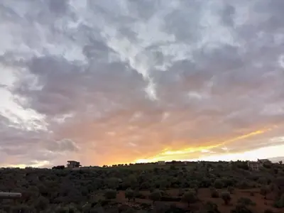 a cloudy sky with the sun setting on a hill at Happy farm in Umm Jawzah
