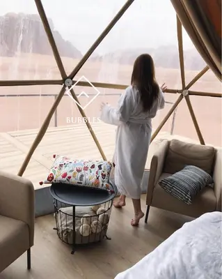 a woman in a white robe looking out of a window at BUBBLES LUXURY CAMp in Wadi Rum