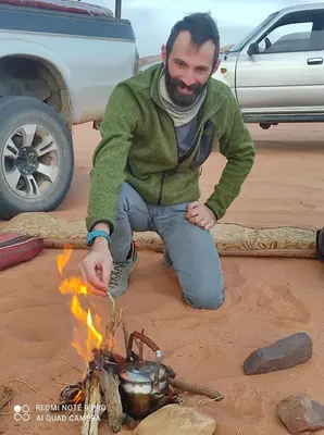 a man sitting next to a fire in the sand at Oasis of Civilizations Camp in Wadi Rum
