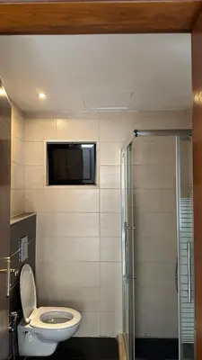 a bathroom with a toilet and a television on the wall at Modern 2BR Apartment in Deir Ghbar in Amman