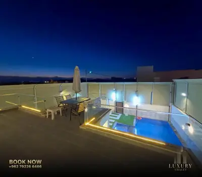 a rooftop patio with a table and a pool at night at Farm Luxury in Shūnat Nimrīn