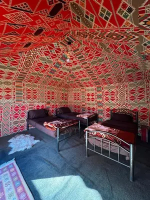 a room with two beds in front of a red wall at Wadi Rum Bedouin in Wadi Rum