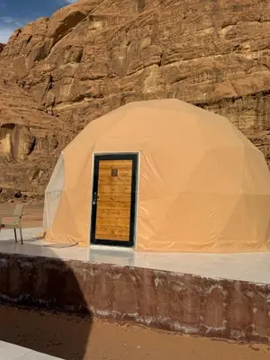 a tent with a wooden door in front of a cliff at Wadi Rum Al-Hadi camp in Disah