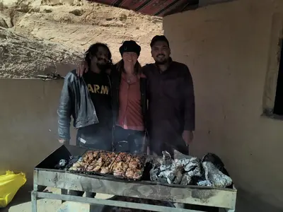 three people standing next to a grill with meat at Bedouin Family Camp in Al Ḩayy