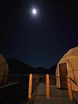 a full moon over some domes at night at Amjad Rum Camp in Disah