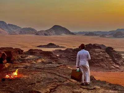 a man standing next to a fire in the desert at Wadi Rum Heritage Camp in Wadi Rum
