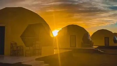 a sunset over domes with the sun in the background at Desert Stars Bubble Camp Wadi Rum in Wadi Rum