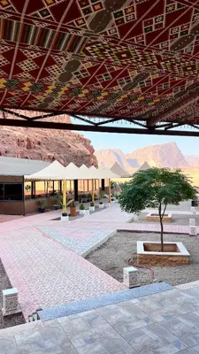 a courtyard with a tree and a building with mountains at Wadi Rum Desert Memory in Wadi Rum