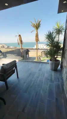a patio with a bench and palm trees and the ocean at LP chalet deadSea view in Sowayma