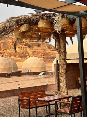 a table and benches under an umbrella in the desert at Rum Ronza Luxury Camp in Maḩaţţat Dīsah