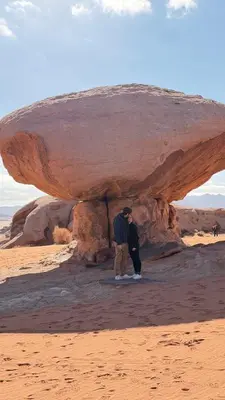 two people standing under a rock in the desert at HALA RUM Luxury camp & Bubbles Hotel in Disah