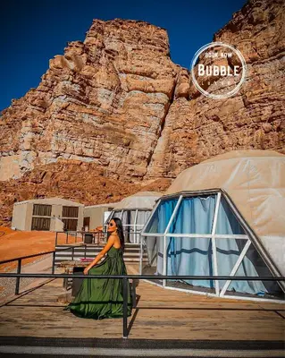 a woman in a green dress standing next to two domes at WADi RUM BUBBLE in Wadi Rum