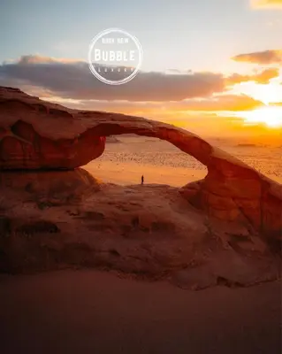 a person standing on the beach under an arch in the sand at WADi RUM BUBBLE in Wadi Rum