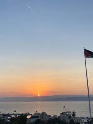 a sunset over the ocean with a flag at Avatar Hotel-Aqaba in Aqaba