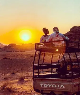 two people sitting on the back of a vehicle watching the sunset at Starlit Wadi Rum camp in Wadi Rum