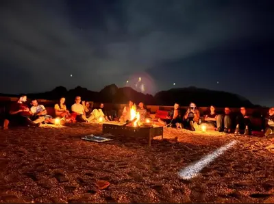 a group of people sitting around a bonfire at night at Starlit Wadi Rum camp in Wadi Rum