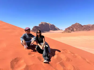 a man and woman sitting on a sand dune in the desert at Magic Cave Night Tours in Wadi Rum