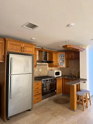 a kitchen with a stainless steel refrigerator and wooden cabinets at Deir Ghbar apartment 116 in Amman