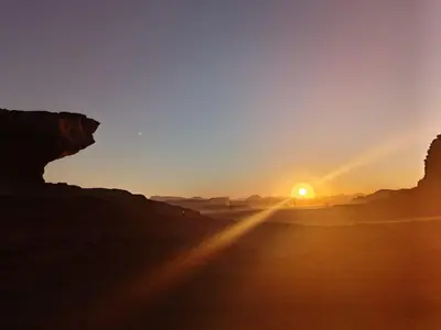 a sunset in the desert with the sun setting at DESERT PULSE lUXURY CAMP in Wadi Rum