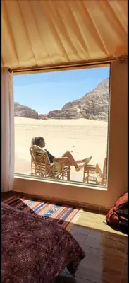 a person laying in a chair looking out of a window at the desert at Essam camb in Disah