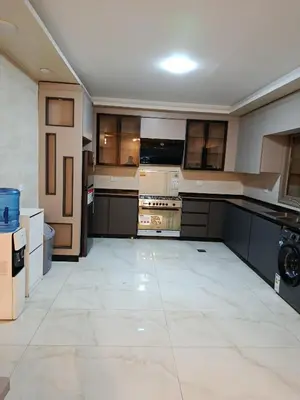 a large kitchen with black cabinets and a white tile floor at شقه مفروشه للايجار بجانب الكارفور اربد in Irbid