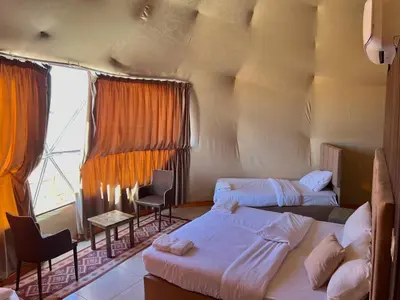 a room with two beds and chairs and a window at Golden Dunes Camp Wadi Rum in Wadi Rum