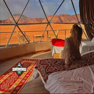 a woman sitting on a bed looking out at the desert at RUM ELARA lUXRY CAMP in Wadi Rum