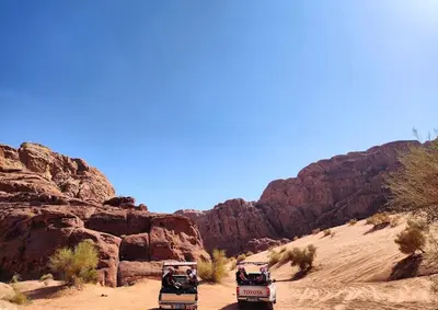 two vehicles driving down a dirt road in the desert at Bedouin Whispers Camp wadirum in Wadi Rum