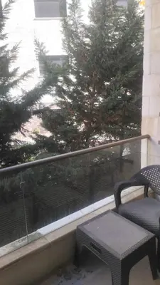 a chair and a table on a balcony with a tree at Chic 2-Bedroom - Fully Furnished in Amman