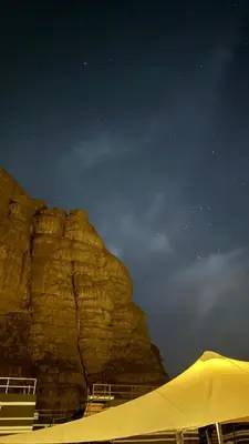 a tent in front of a large mountain at night at Wadi Rum Royal Camp in Disah