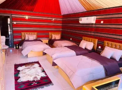 a room with four beds in it with red walls at Wadi Rum Nomad Way Camp in Wadi Rum
