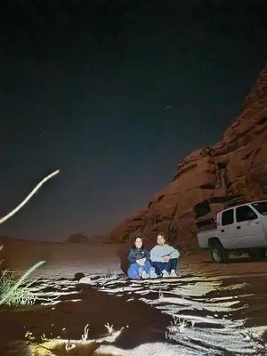 two people sitting on a rock next to a truck at Sultan Camp Wadi Rum in Wadi Rum