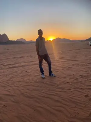 a man standing in the desert with the sunset in the background at Sultan Camp Wadi Rum in Wadi Rum