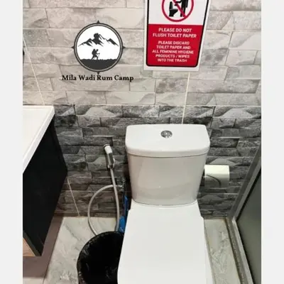 a white toilet in a bathroom with a sign at Mila Wadi Rum Camp in Wadi Rum